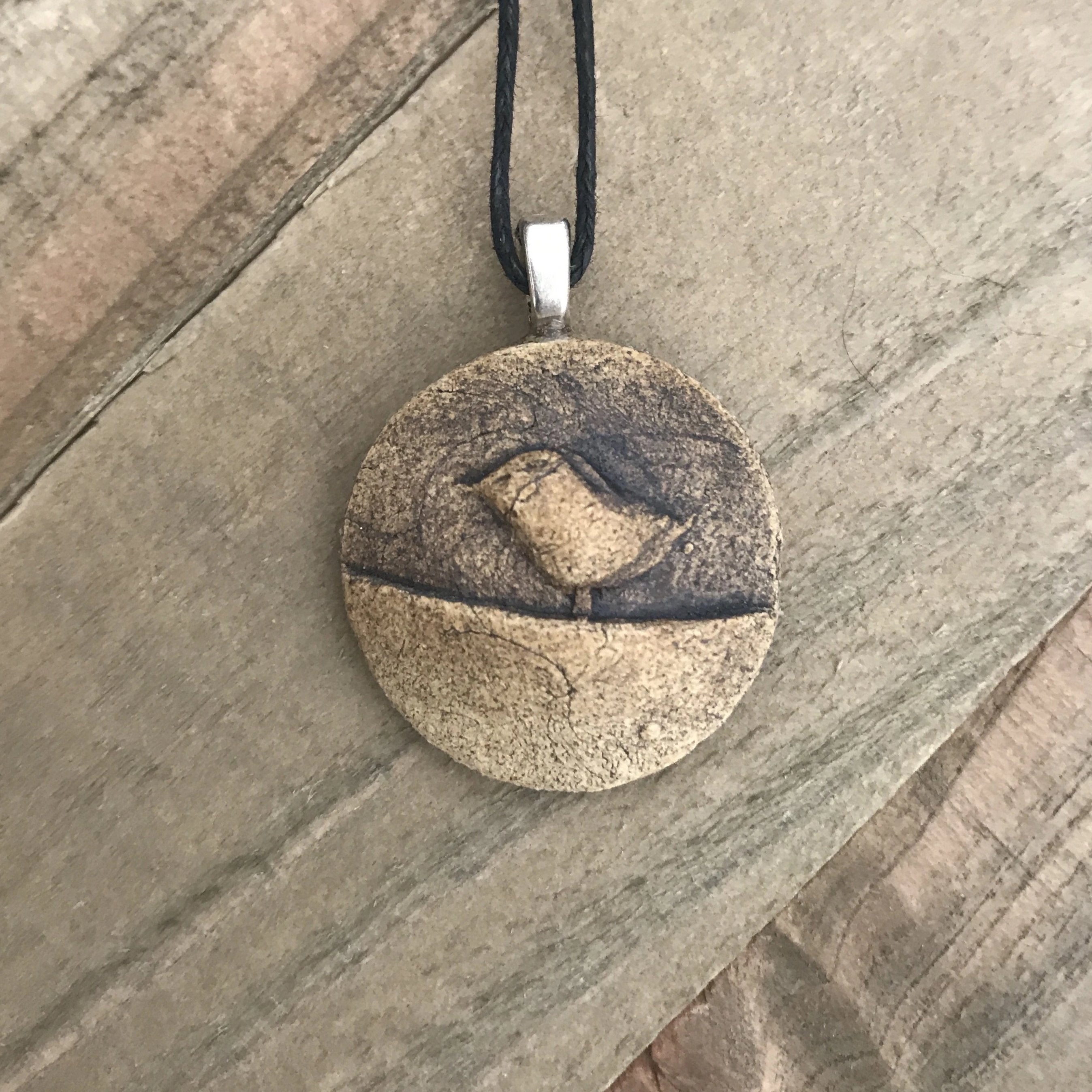 Round pendant necklace with bird. Made of clay, brown color.
