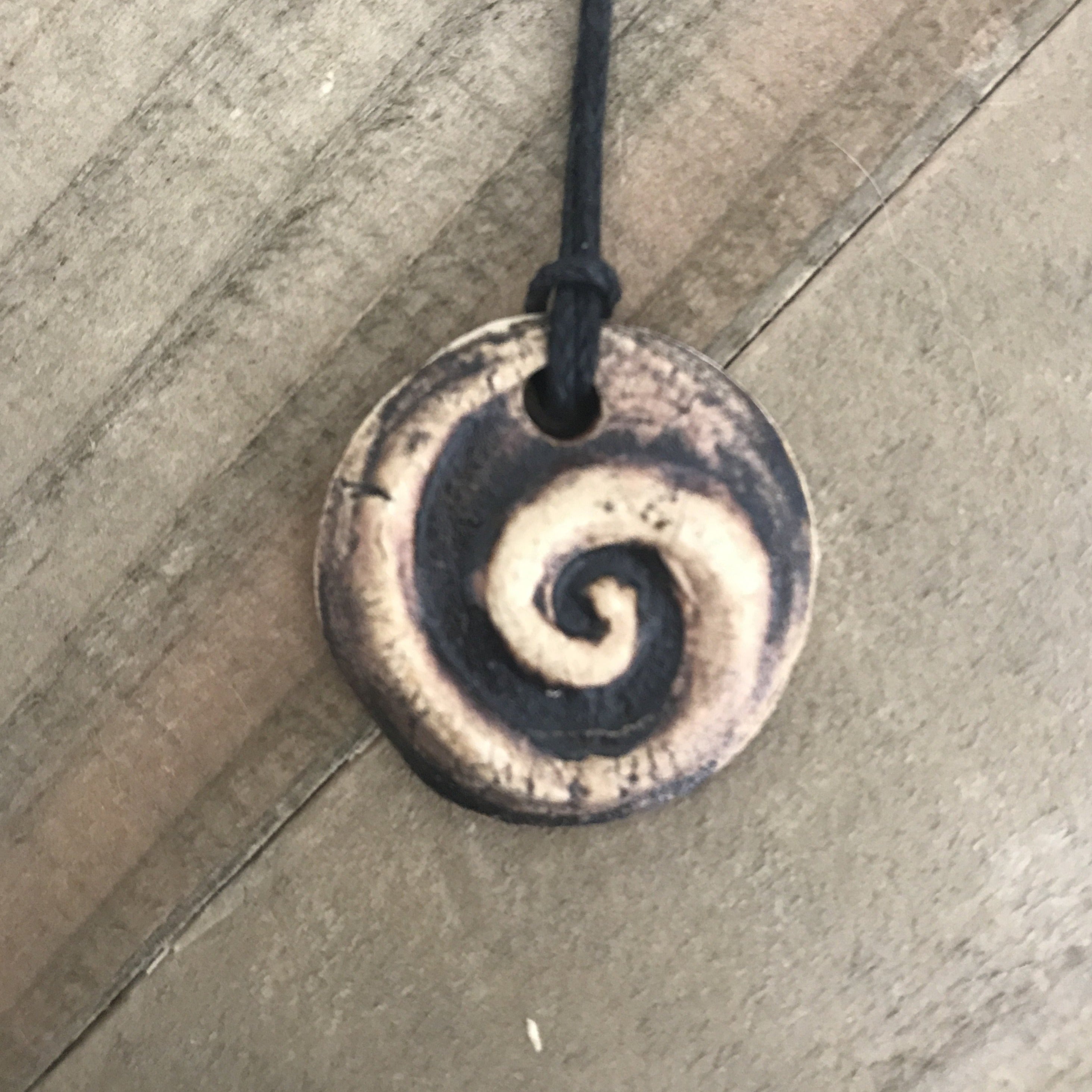 Round pendant necklace with koru spiral. Made of clay, brown color.